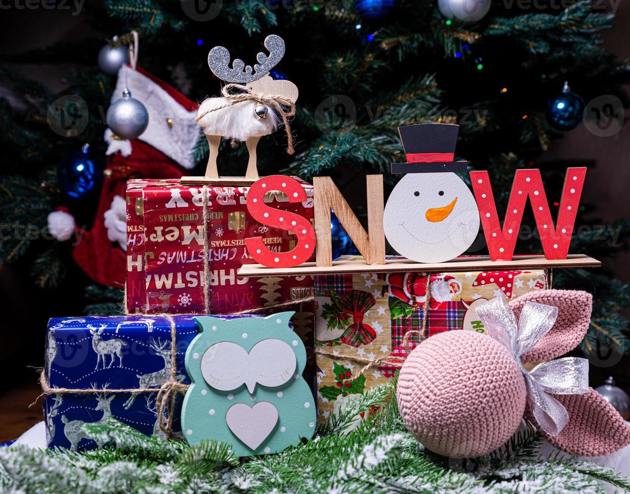 The inscription snow from a tree on a New Year's. On the spruce branches against the background of a snow cover are New Year's blue, white balls with spruce cones and a box with a gift. Christmas photo