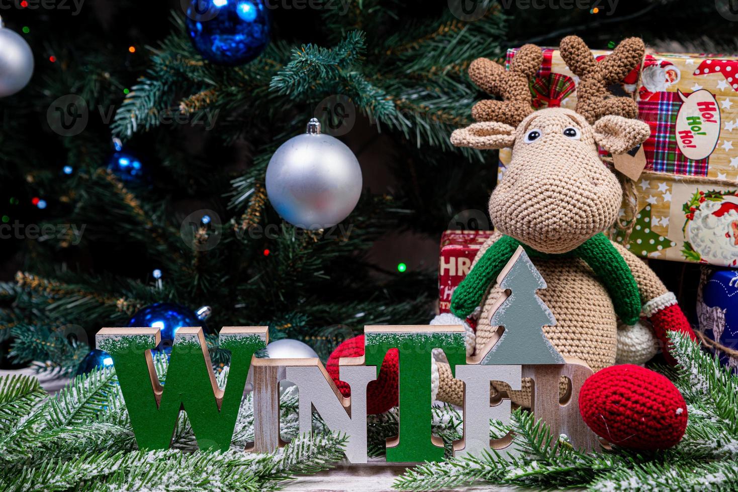 The inscription winter from a tree on a New Year's. On the spruce branches against the background of a snow cover are New Year's blue, white balls with spruce cones and a box with a gift. Christmas photo