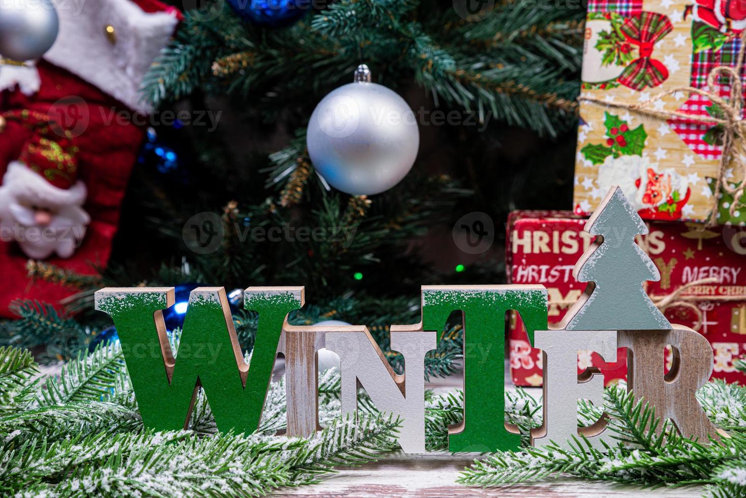 la inscripción invierno de un árbol en año nuevo. en las ramas de abeto contra el fondo de una capa de nieve hay bolas azules y blancas de año nuevo con conos de abeto y una caja con un regalo. Navidad foto