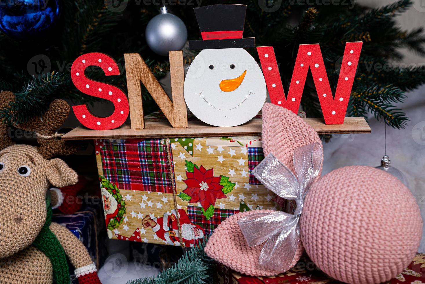 The inscription snow from a tree on a New Year's. On the spruce branches against the background of a snow cover are New Year's blue, white balls with spruce cones and a box with a gift. Christmas photo