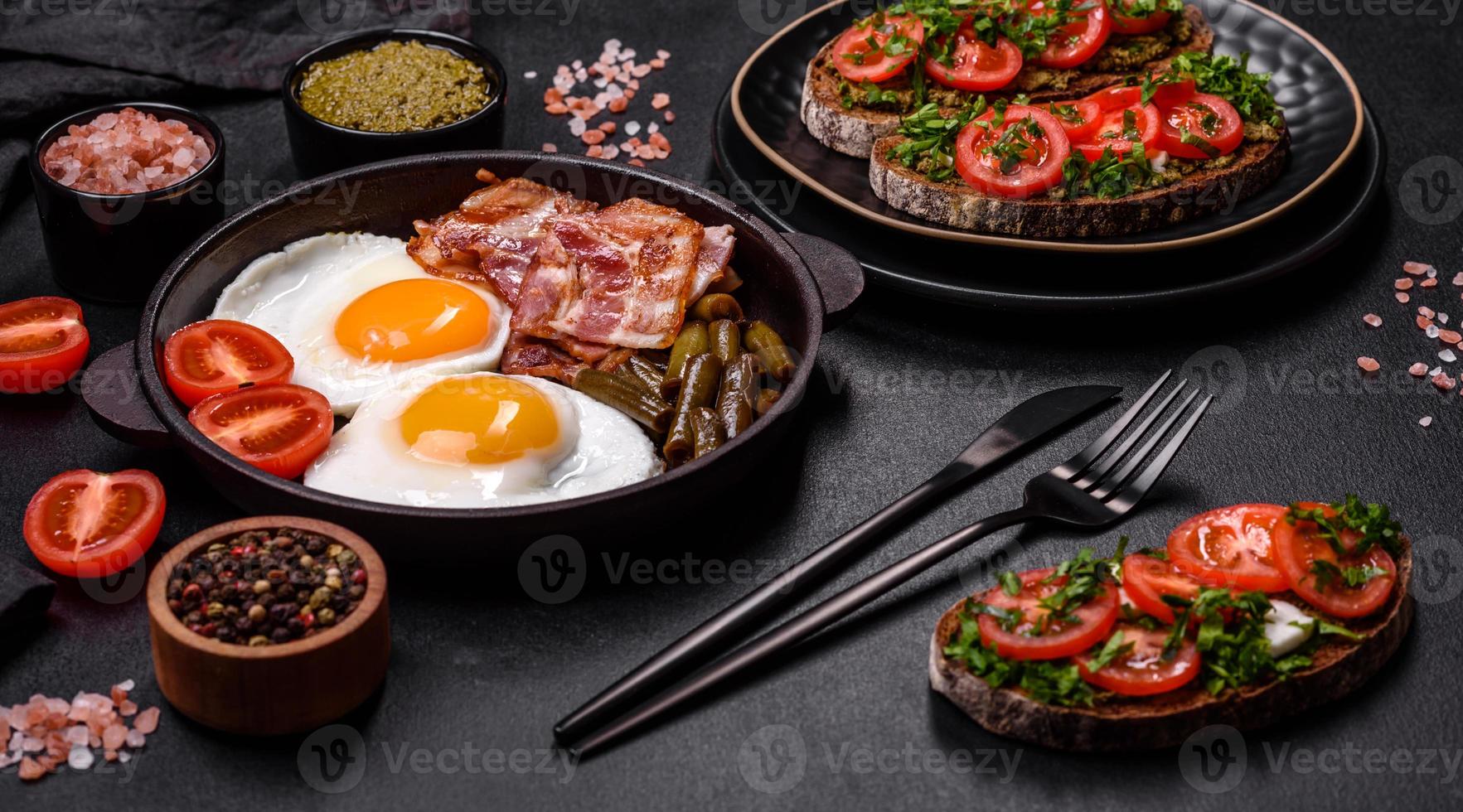 Tasty breakfast consists of eggs, bacon, beans, tomatoes, with spices and herbs photo