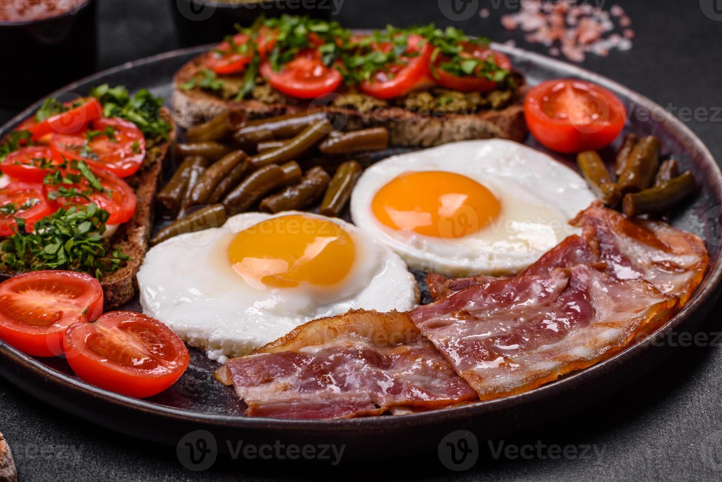 Tasty breakfast consists of eggs, bacon, beans, tomatoes, with spices and herbs photo
