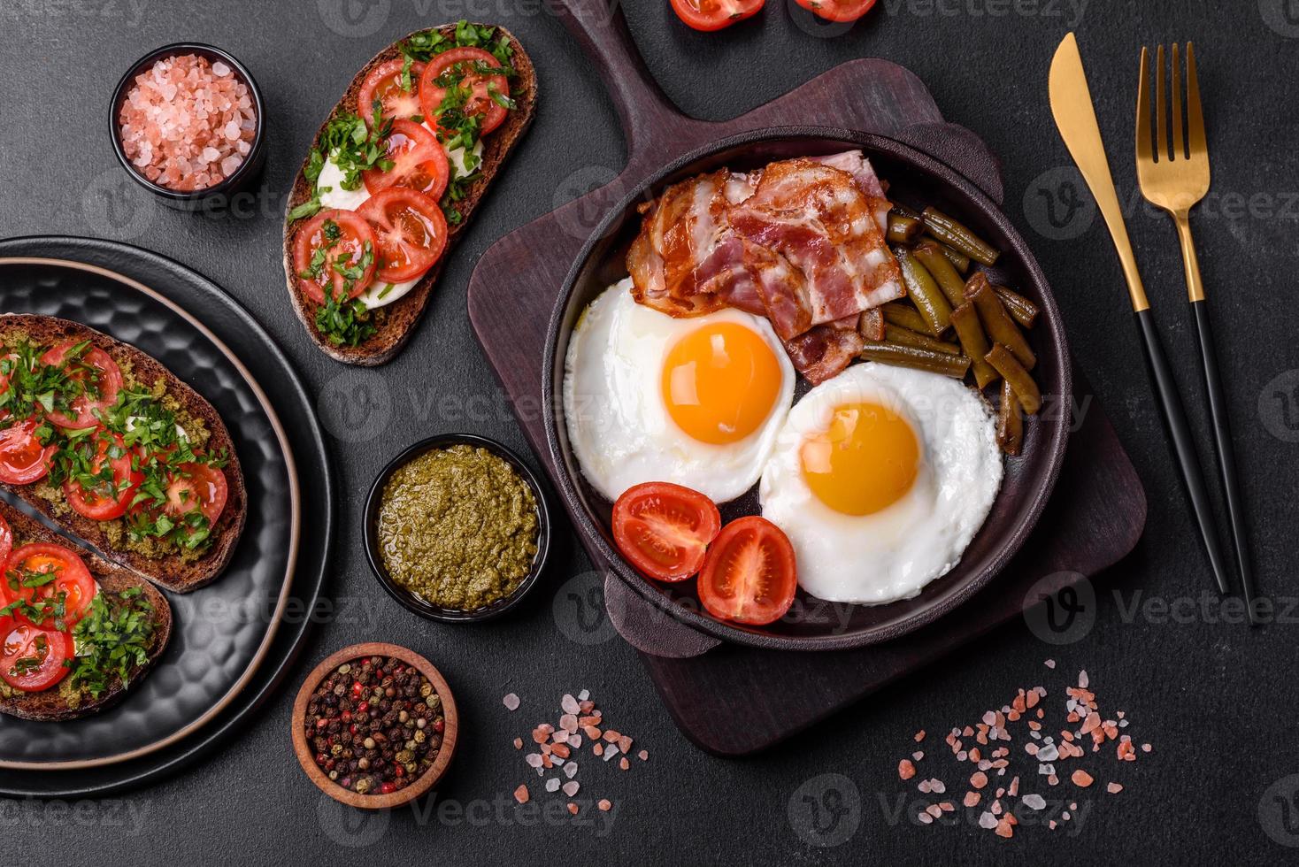 Tasty breakfast consists of eggs, bacon, beans, tomatoes, with spices and herbs photo