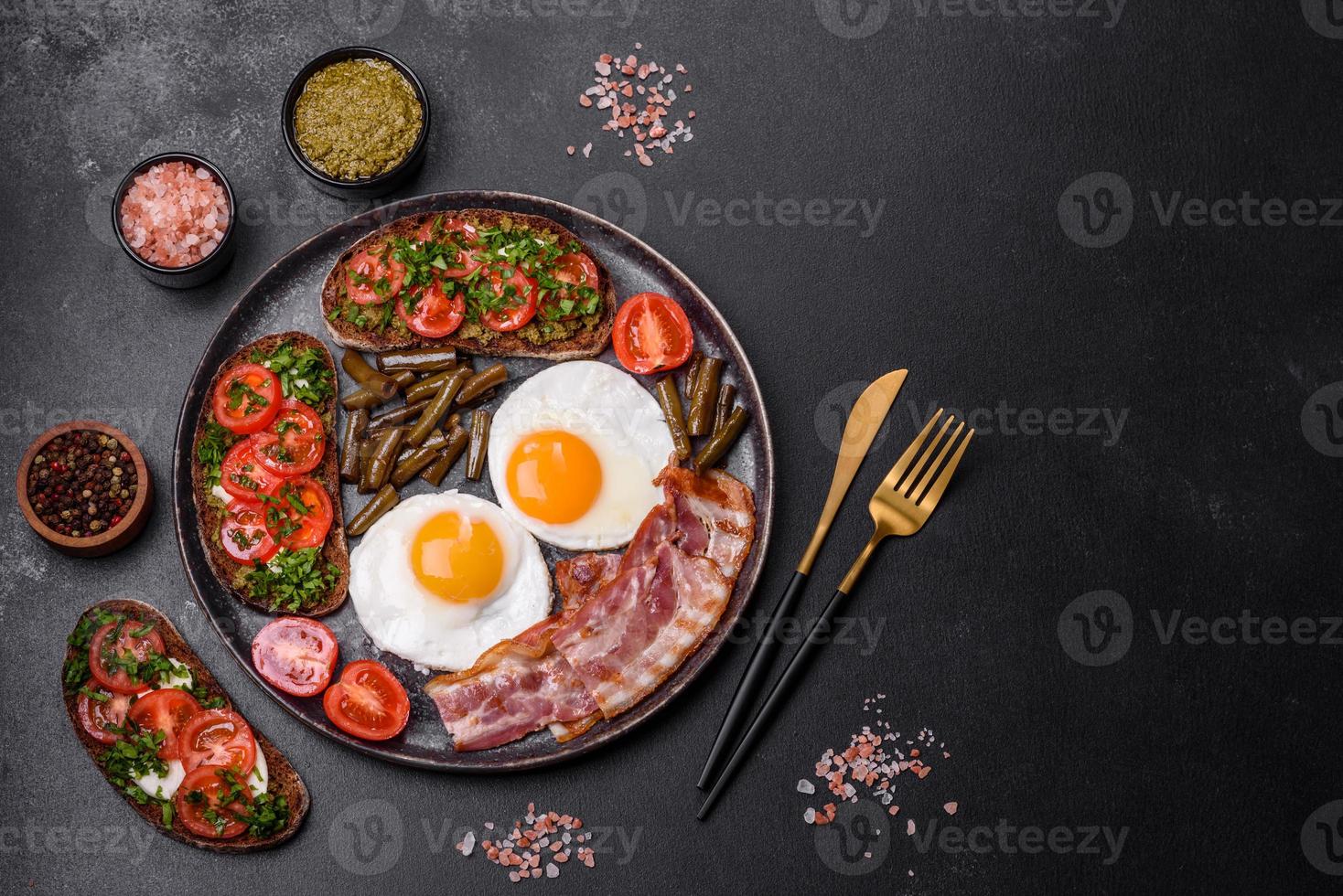 Tasty breakfast consists of eggs, bacon, beans, tomatoes, with spices and herbs photo