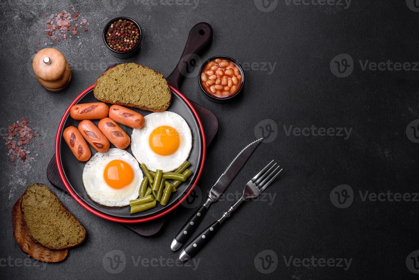 Tasty English breakfast of fried eggs, beans, asparagus, sausages with spices and herbs photo