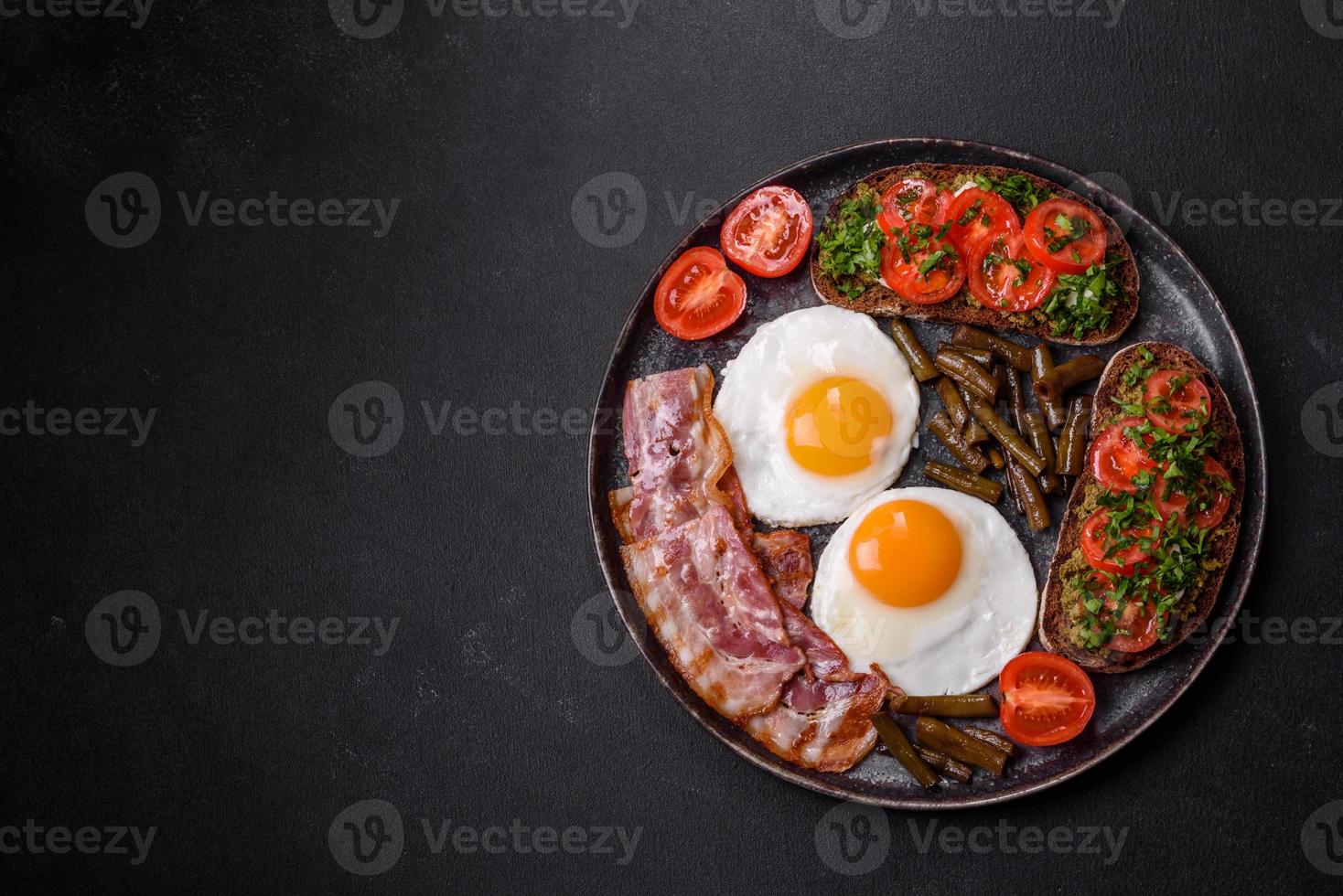 Tasty breakfast consists of eggs, bacon, beans, tomatoes, with spices and herbs photo