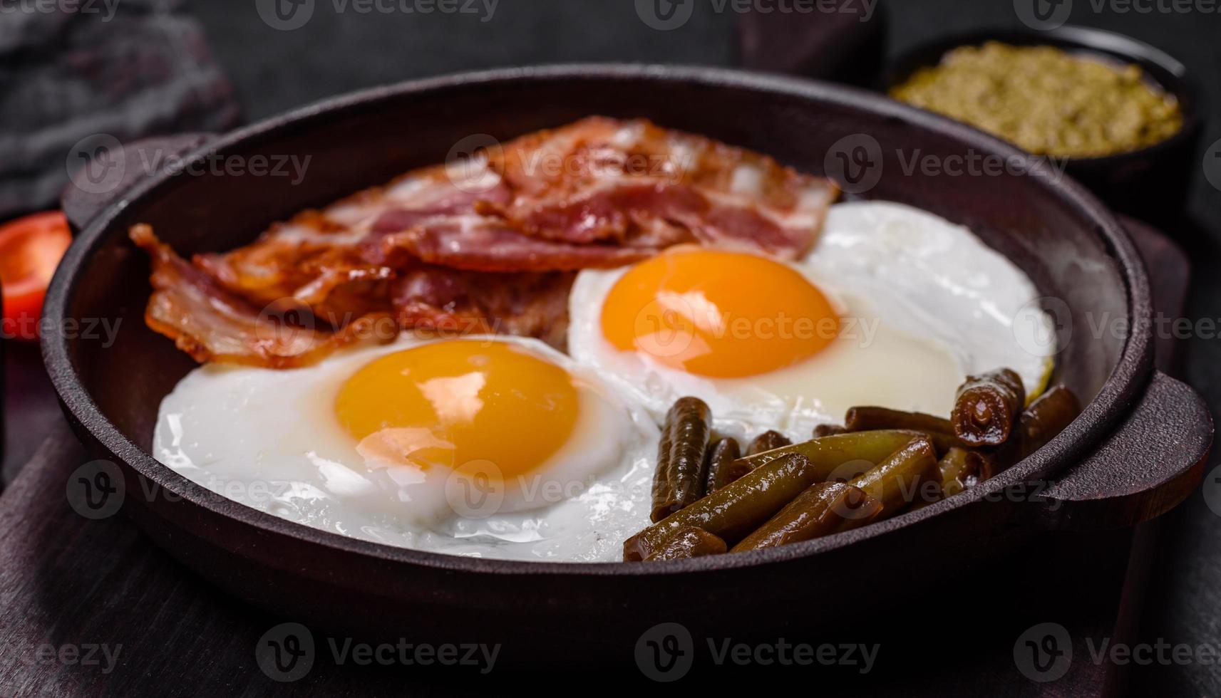 Tasty breakfast consists of eggs, bacon, beans, tomatoes, with spices and herbs photo