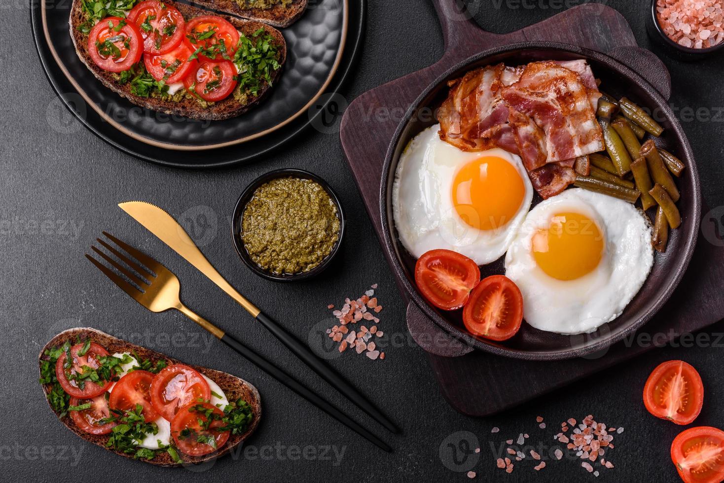 Tasty breakfast consists of eggs, bacon, beans, tomatoes, with spices and herbs photo