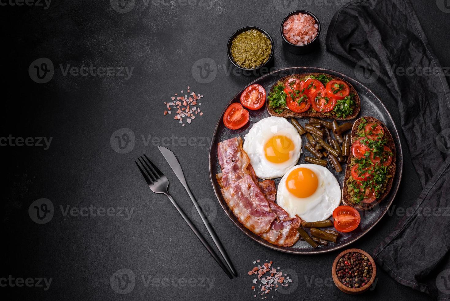 Tasty breakfast consists of eggs, bacon, beans, tomatoes, with spices and herbs photo