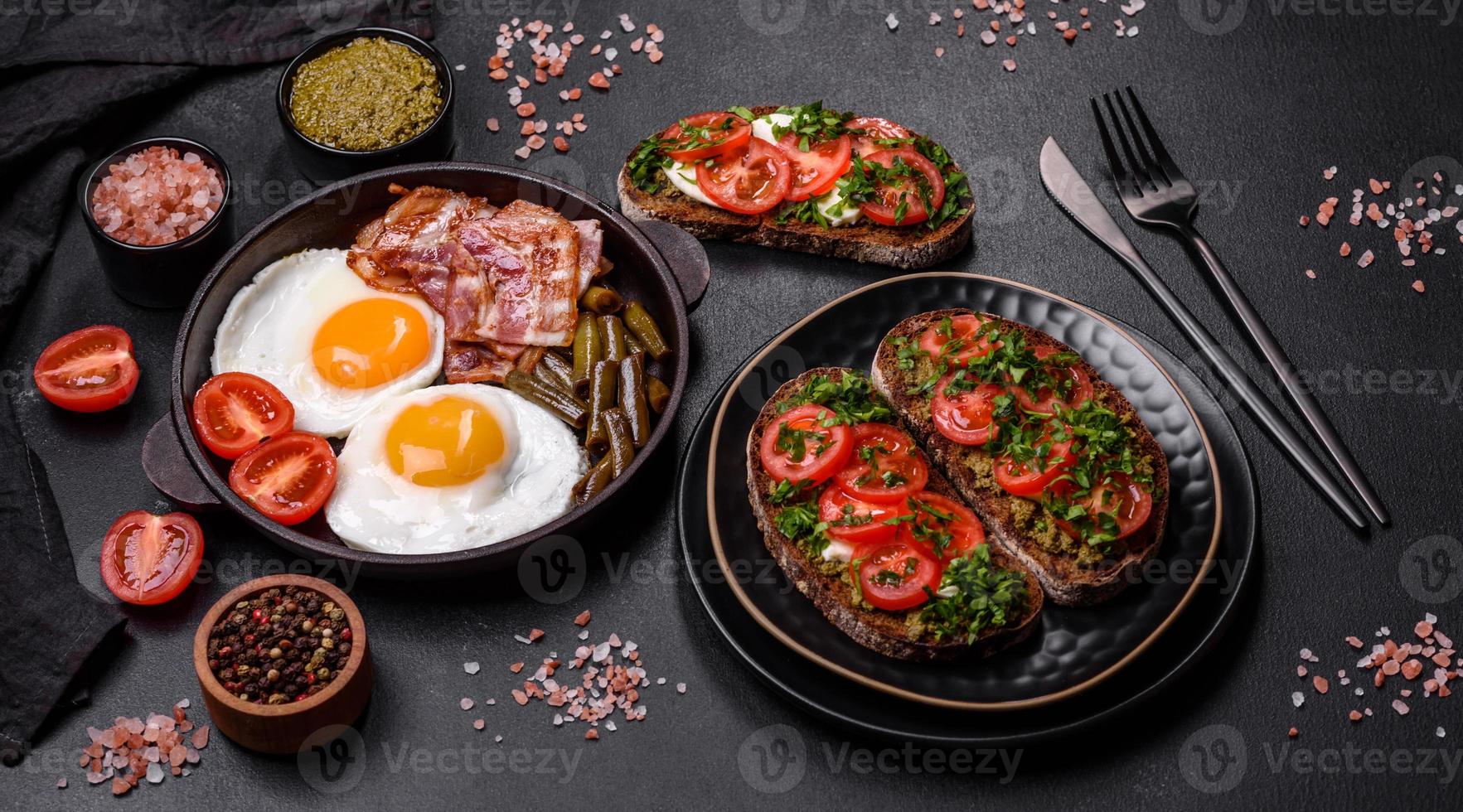 Tasty breakfast consists of eggs, bacon, beans, tomatoes, with spices and herbs photo