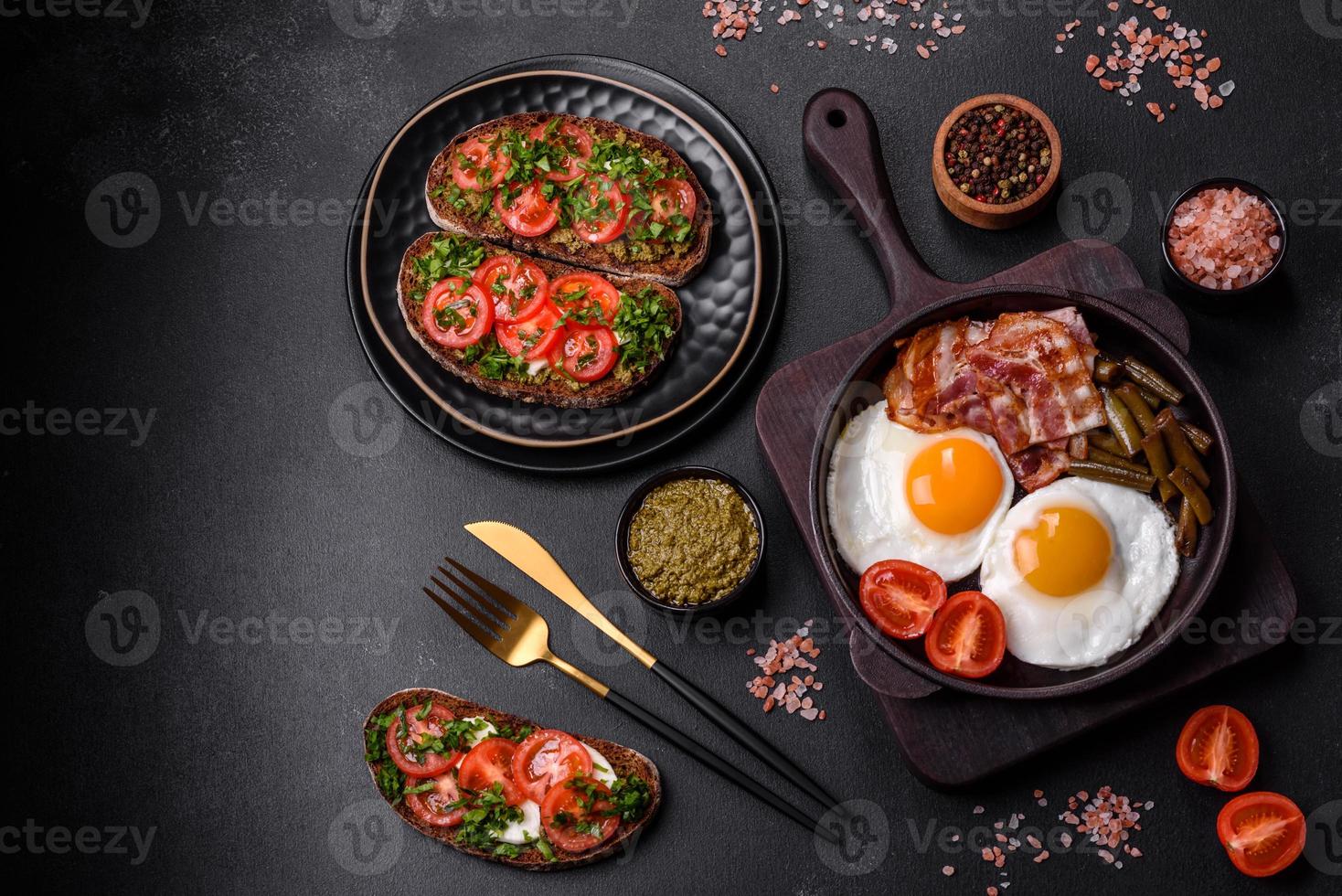 Tasty breakfast consists of eggs, bacon, beans, tomatoes, with spices and herbs photo