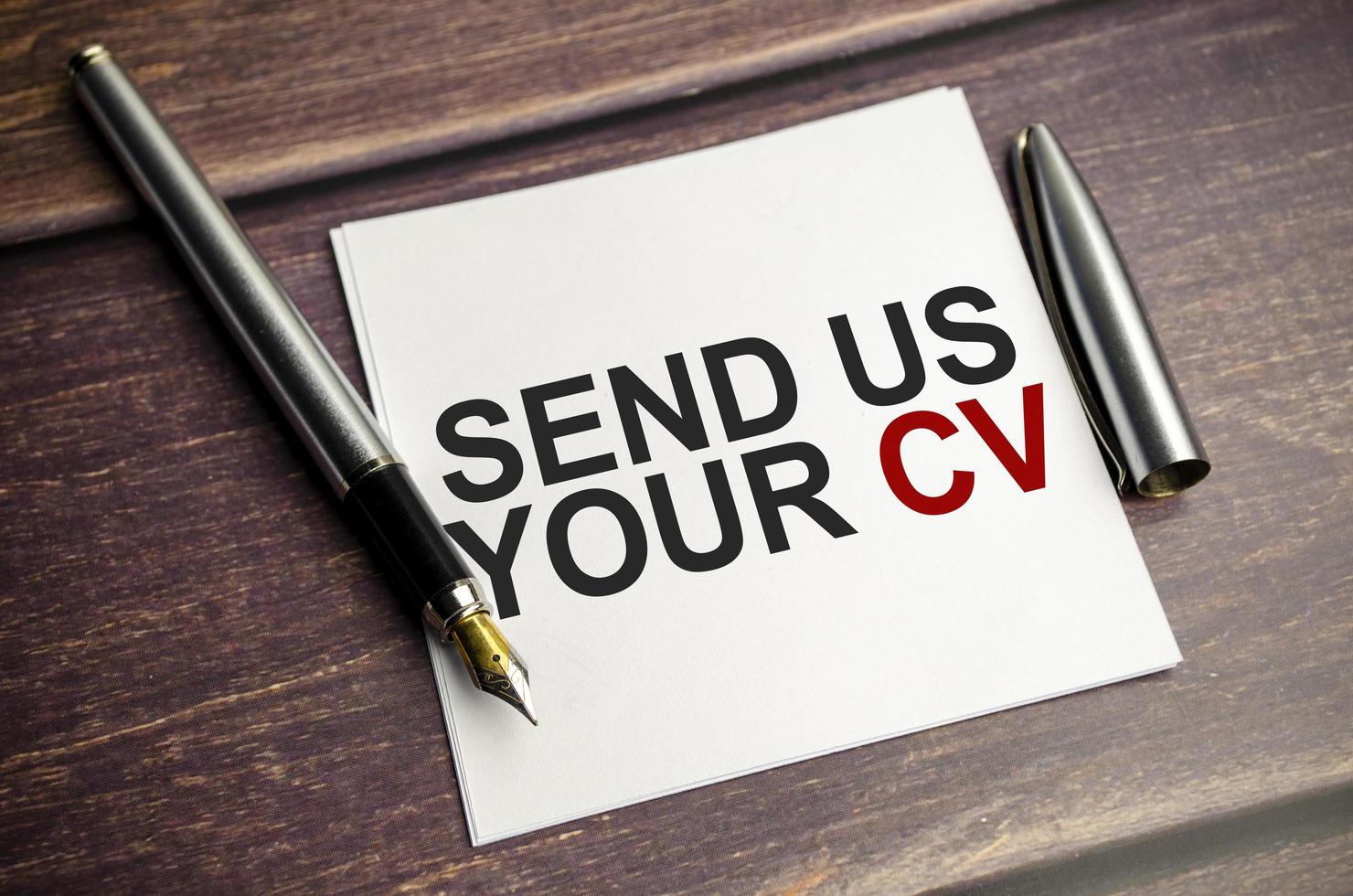 white card with text send us your cv on wooden background photo
