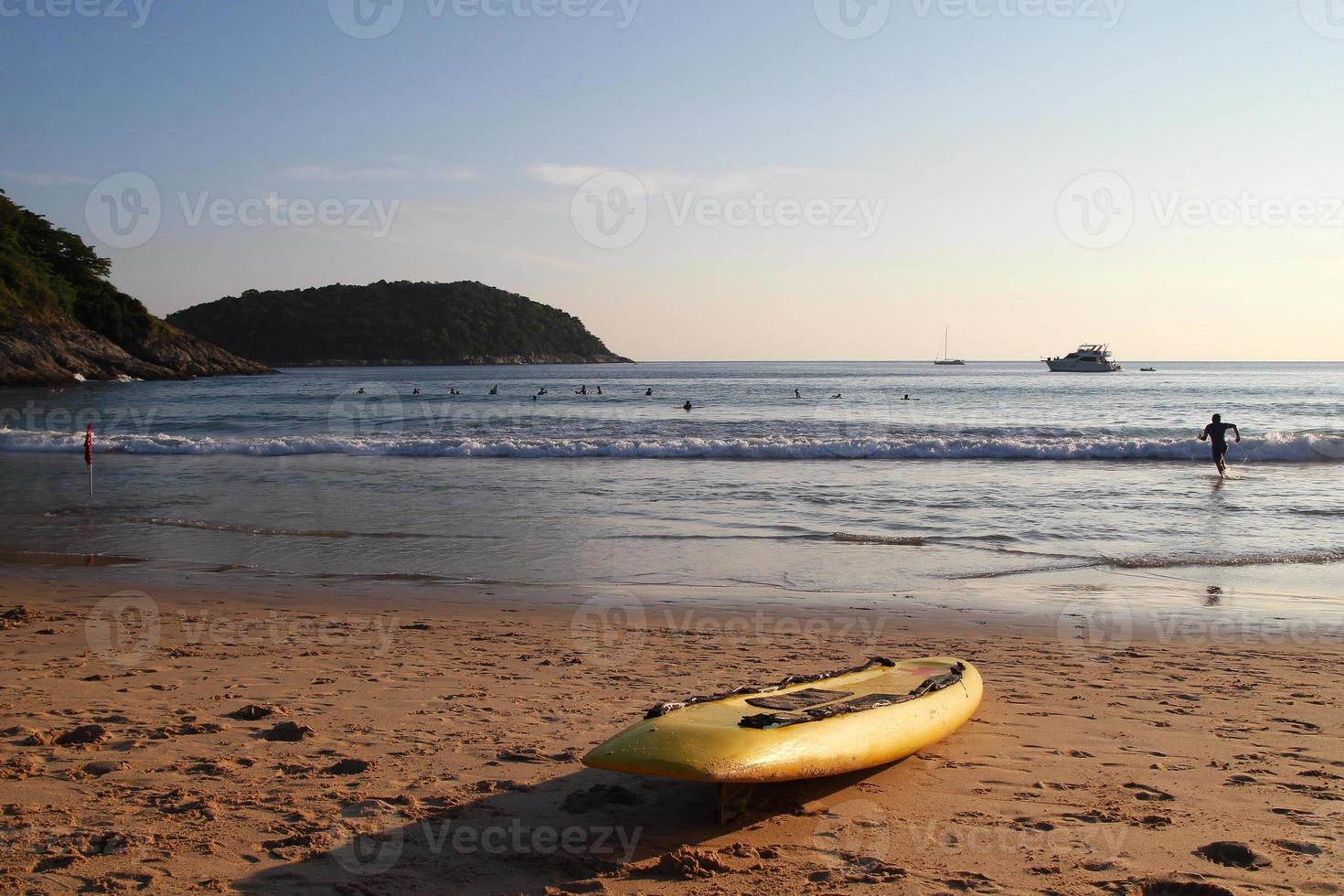 viajar a la isla de phuket, tailandia. tabla de surf amarilla en la playa de arena con mar, cielo azul y una montaña en el fondo. foto