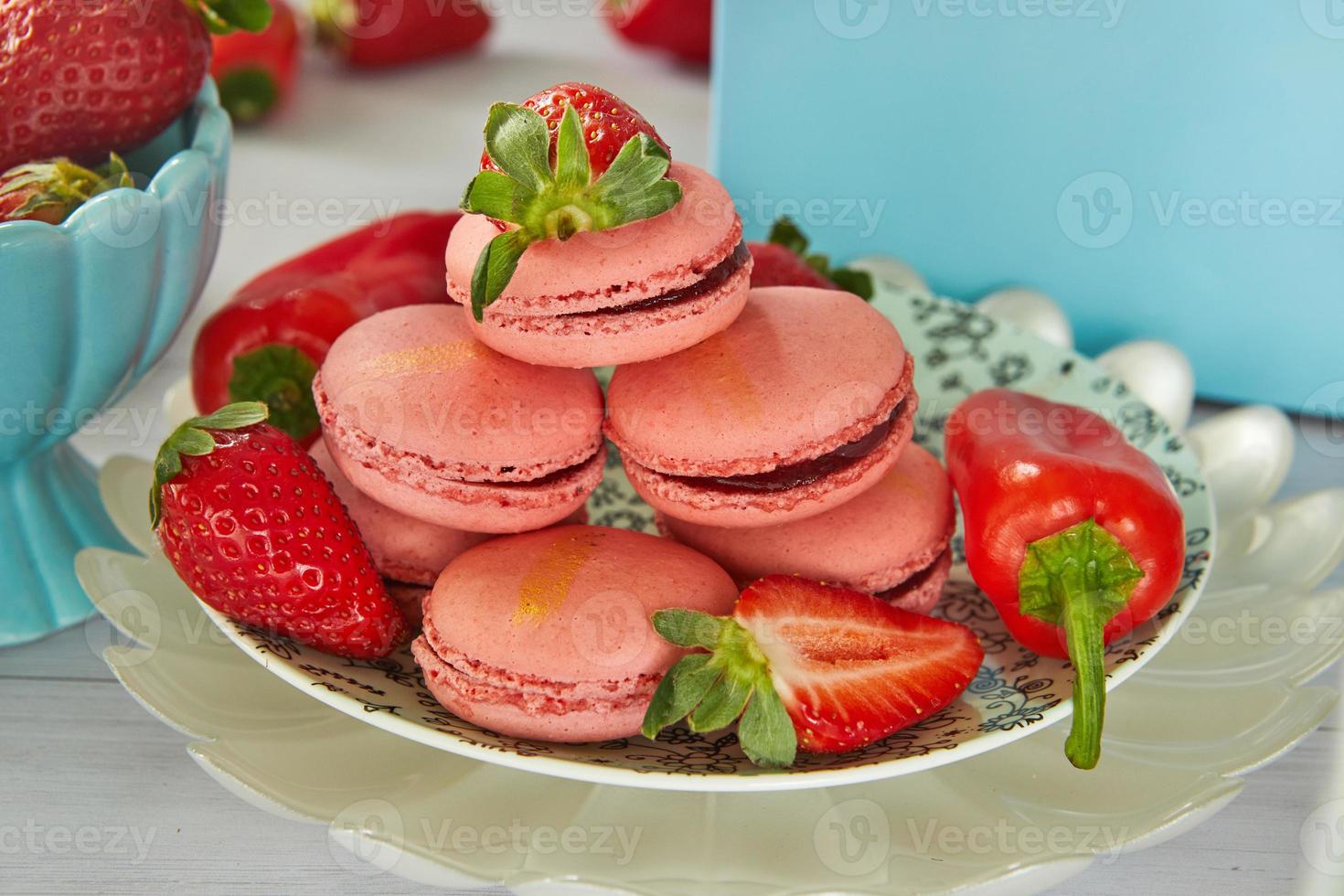 macarons de fresa de color rosa con fresas y pimientos sobre fondo de madera clara foto
