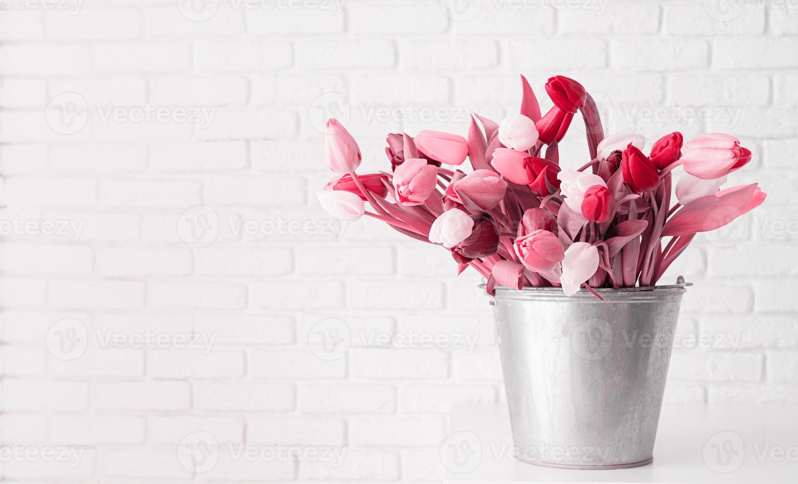 cubo de flores de tulipán sobre fondo de pared de ladrillo blanco tonificado con el color viva magenta del año 2023 foto