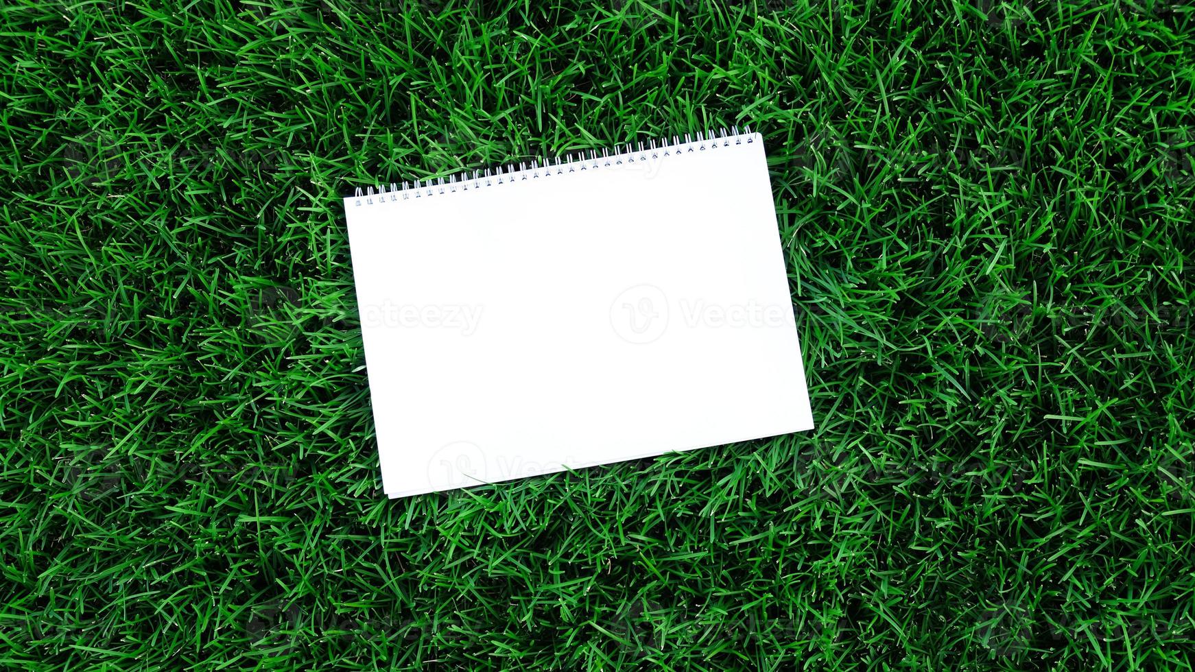 Empty white paper on green grass background. For message flat lay with copy space for text or products presentation. Nature concept, business and lifestyle environment. photo
