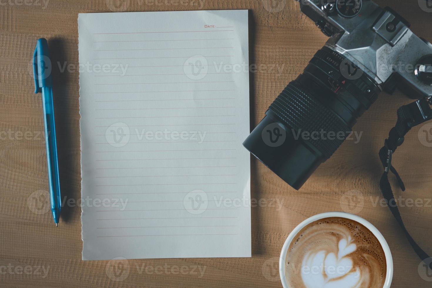 Top view of empty paper, coffee cup, camera and pen on the wooden table photo