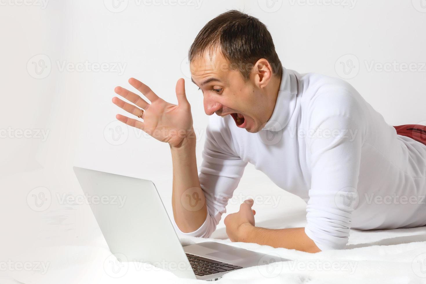 Surfing web at home. Cheerful young man lying on the floor with laptop, isolated over white background photo