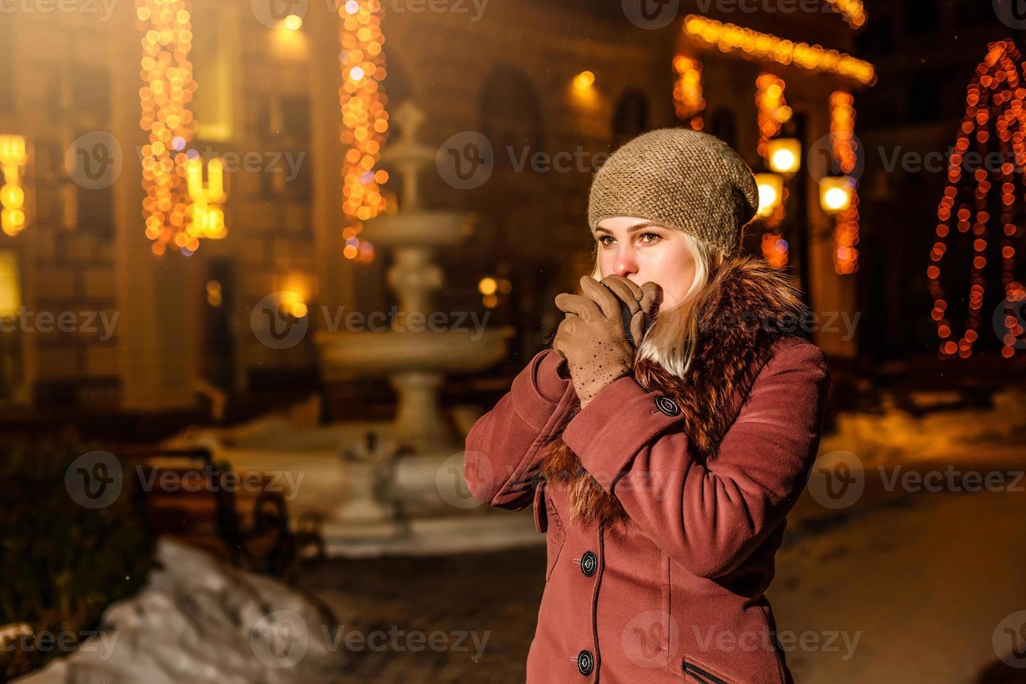 mujer calentándose las manos congeladas. chica se congeló. paisaje de invierno sobre un fondo. noche de navidad calle foto