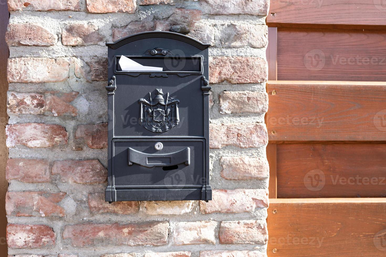 Old steel, iron mail box on stone brick wall, next to wooden fence on building or house door. Home related object, mail box photo