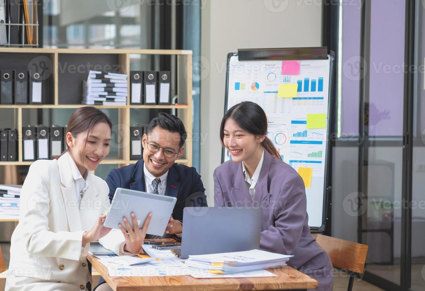 El equipo de negocios asiático está formado por personal de marketing. el contador y el oficial financiero se ayudan mutuamente a analizar las ganancias de la empresa usando tabletas. computadoras portátiles con calculadora, papel cuadriculado y bolígrafos corporativos. foto