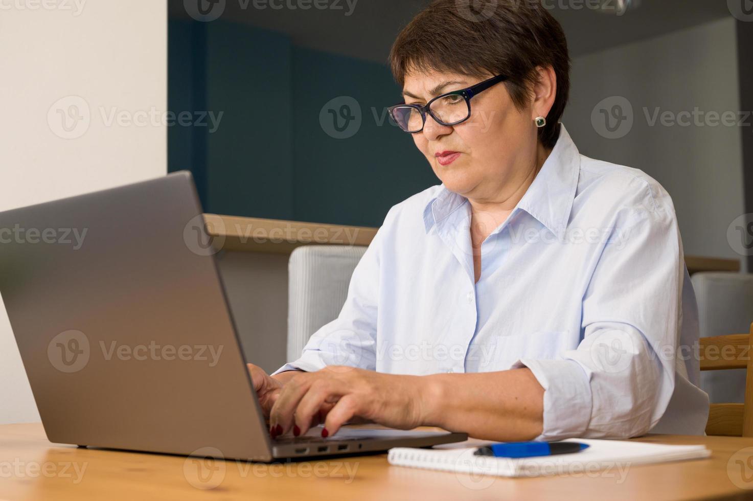 Serious elder woman woking on laptop at home. Business woman. Remote work concept photo