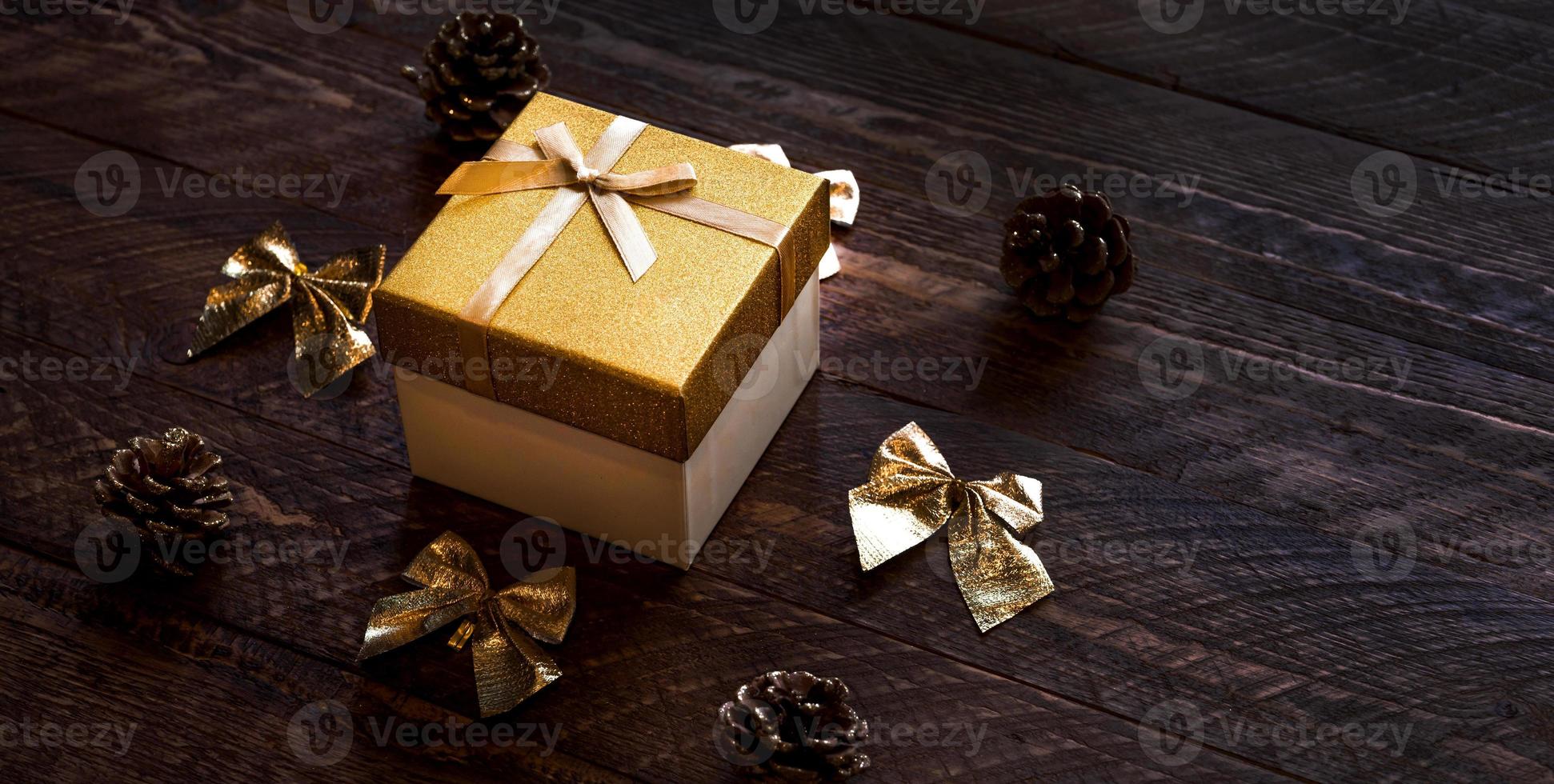 caja de regalo dorada sobre mesa de madera con otros elementos decorativos. banner de vacaciones de invierno con lugar para texto. navidad rústica o año nuevo foto