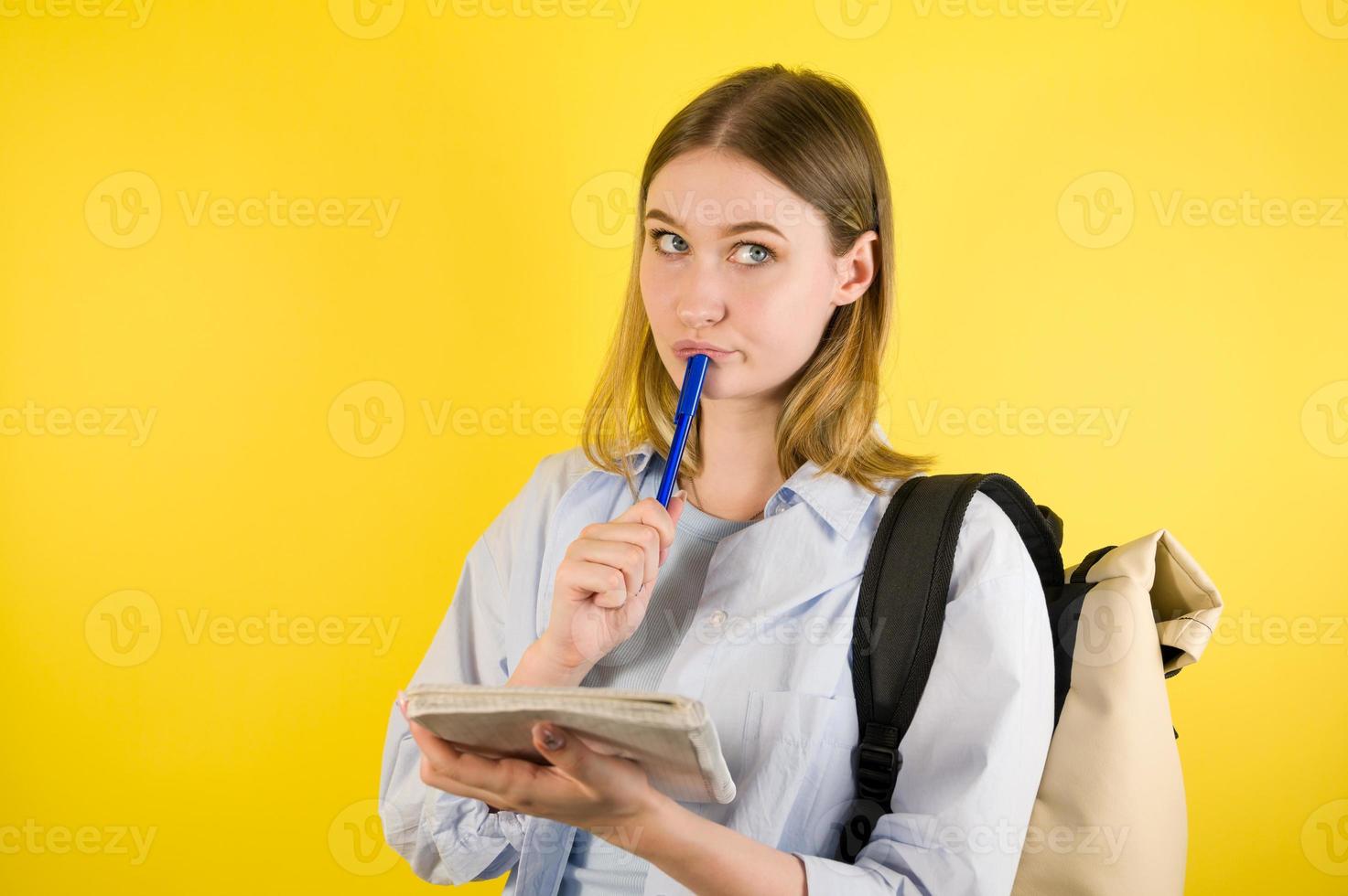 Closeup of a thoughtful caucasian female preparing to take notes in copybook on yellow studio background. Prepare checklist of school or college photo