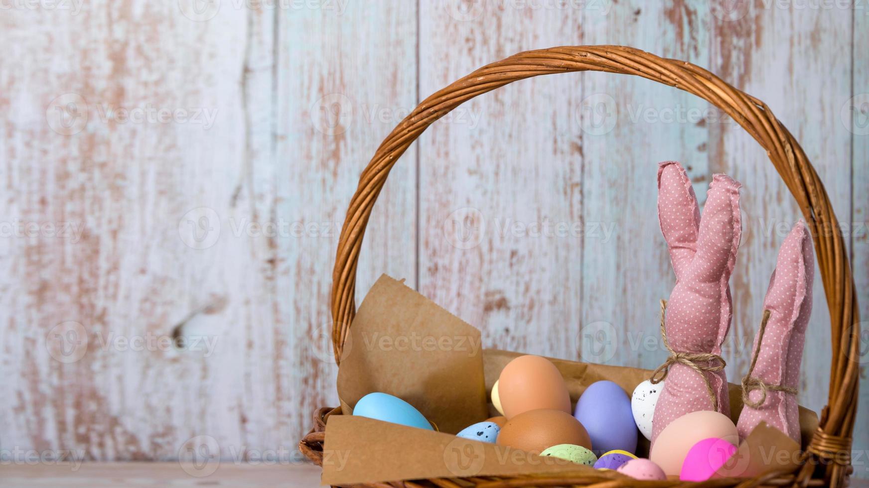 Closeup of pink toy bunnies in the basket full of colorfull eggs. Happy easter banner with place for text photo