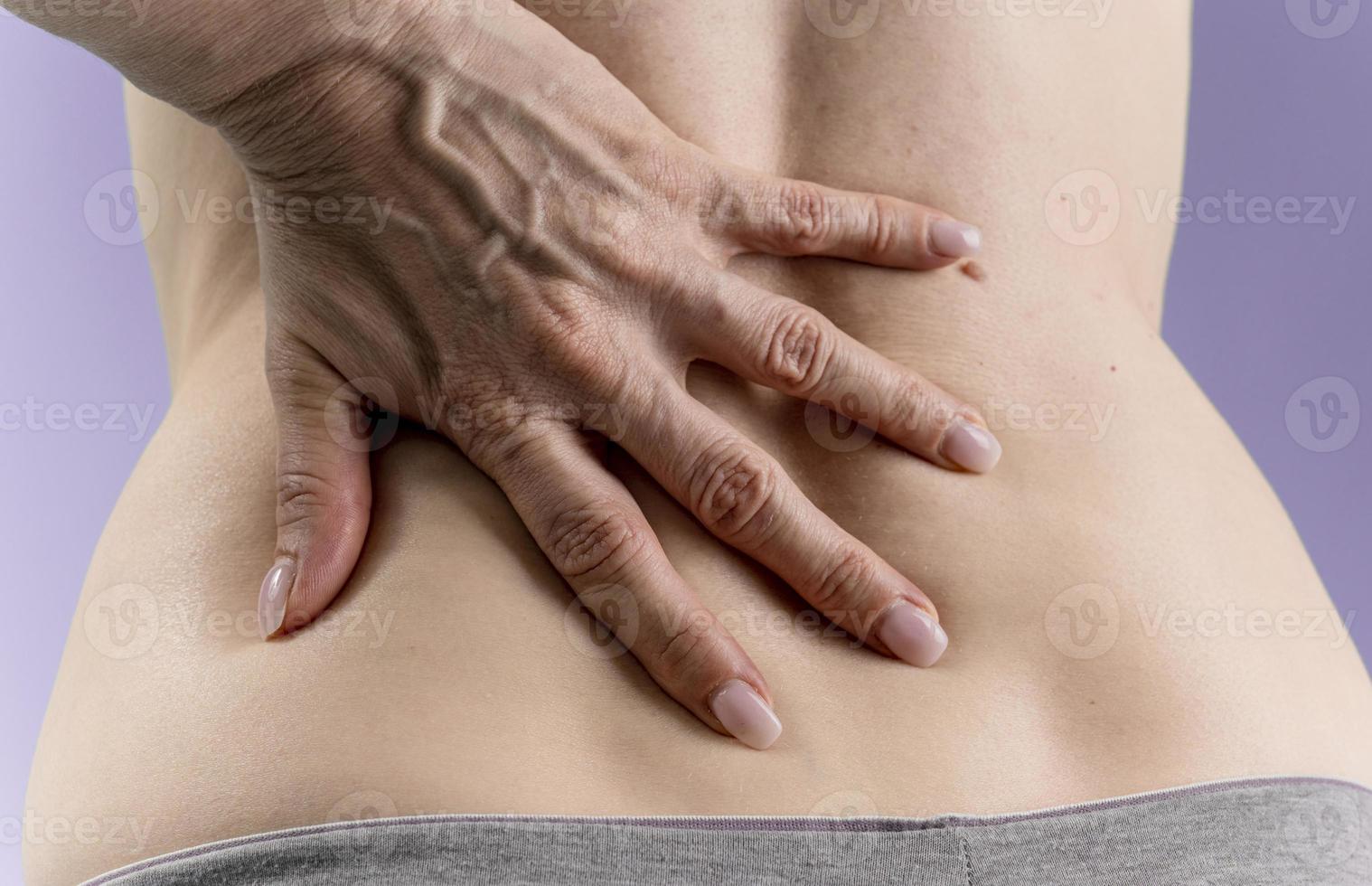 mujer cogida de la mano en la parte baja de la espalda sintiendo un gran dolor. aislado sobre fondo morado foto
