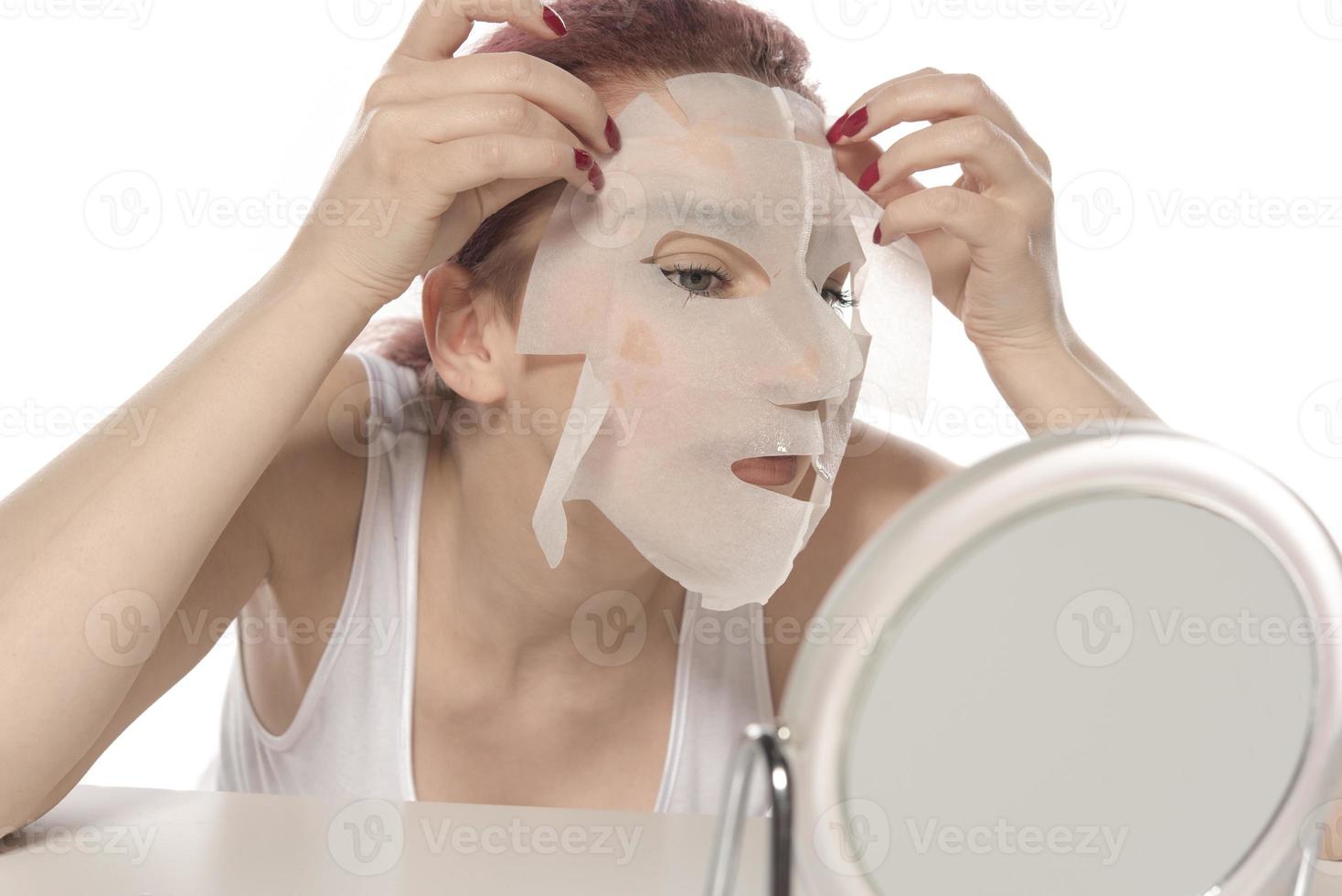 Face care and beauty treatments. Woman with a sheet moisturizing mask on her face isolated on white background photo