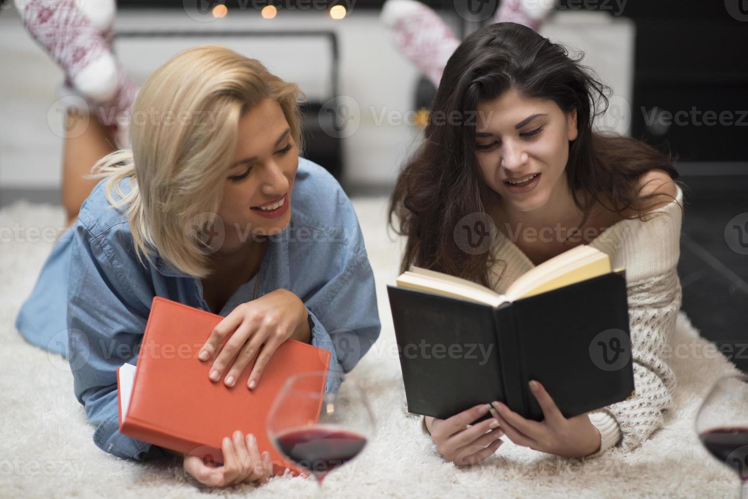 dos amigas leyendo un libro y bebiendo vino tinto junto a una chimenea. concepto de estilo de vida. foto