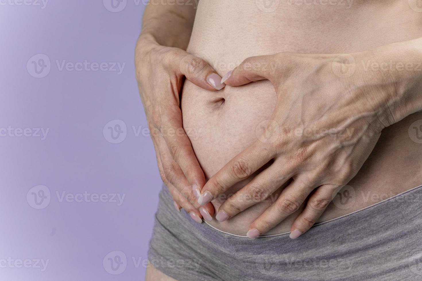 Pregnant woman holds hands on belly on a blue background. Pregnancy, maternity, preparation and expectation concept. Close-up, indoors. Beautiful tender mood photo of pregnancy.