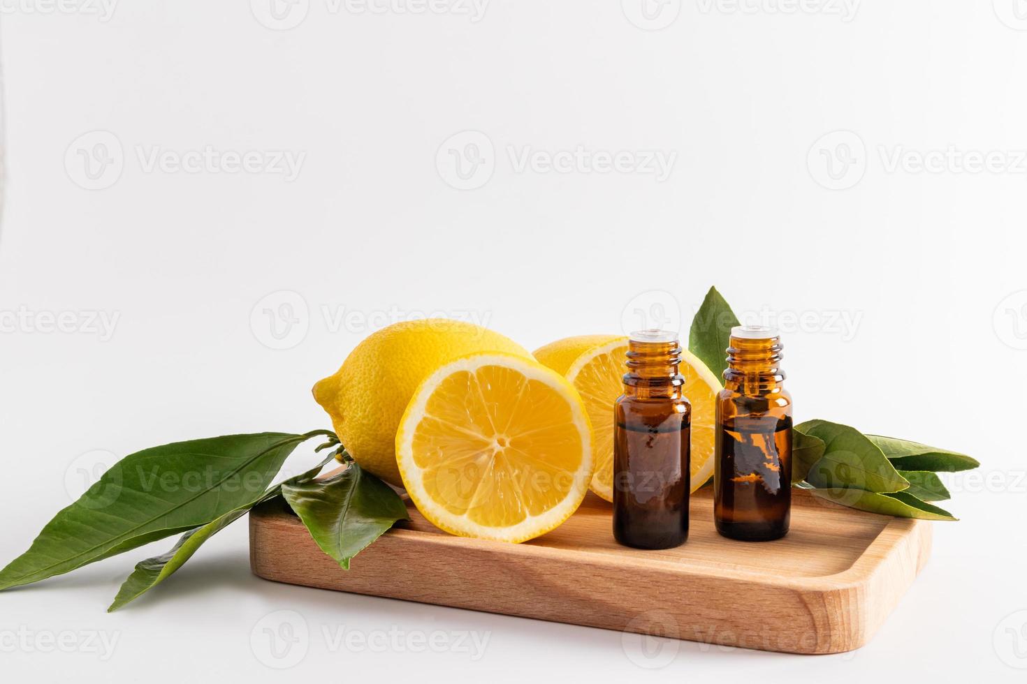 front view of two glass medical bottles with lemon essential oil on a wooden tray among ripe fruits. spa. aromatherapy. relaxation. white background. photo