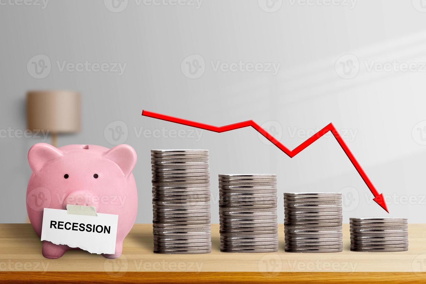 a piggy bank with a sticky note that says recession and a pile of coins from high to low and a graph arrow showing a downtrend photo