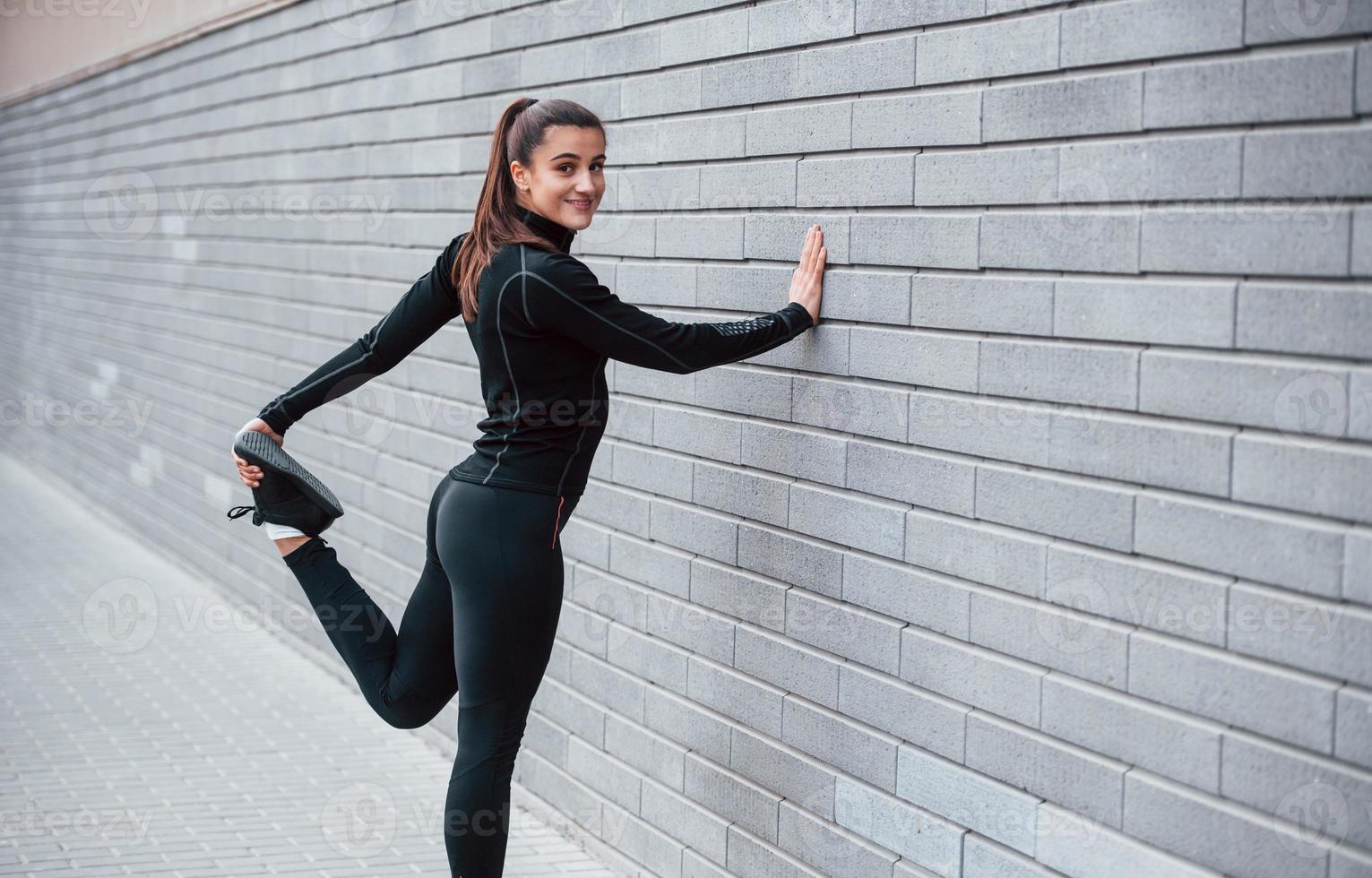 Ladrillo alfiler Hija joven deportiva en ropa deportiva negra al aire libre haciendo  estiramientos cerca de la pared gris 15287811 Foto de stock en Vecteezy