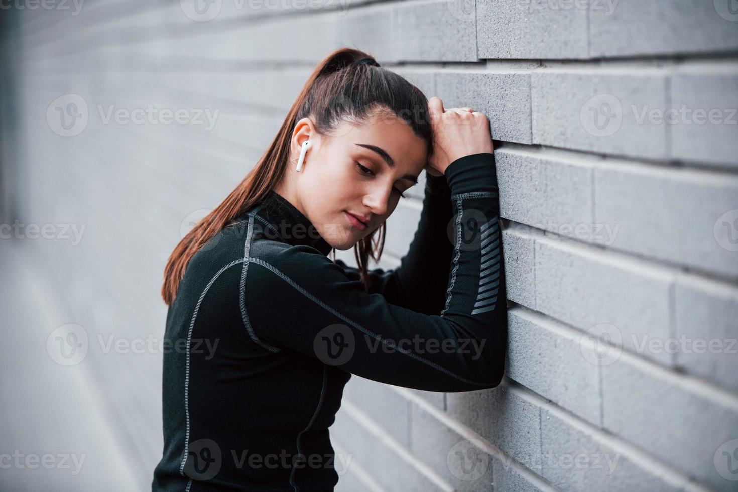 Young sportive girl in black sportswear outdoors near gray wall photo