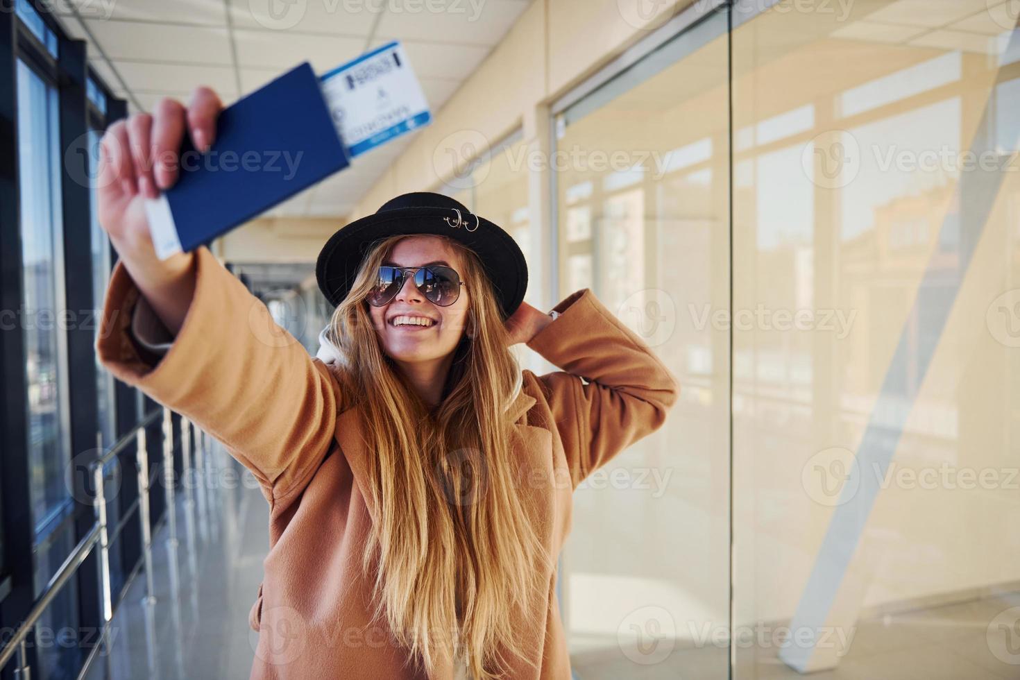 Young female passenger in warm clothes showing tickets in airport hall photo