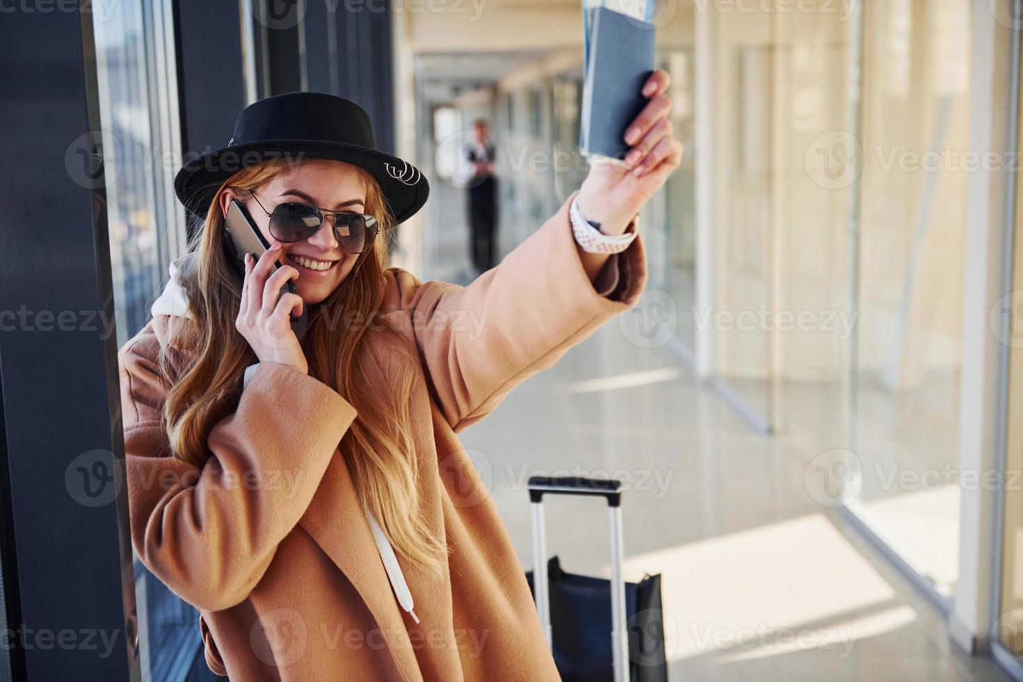 Young woman in sunglasses, warm clothes and hat standing indoors in