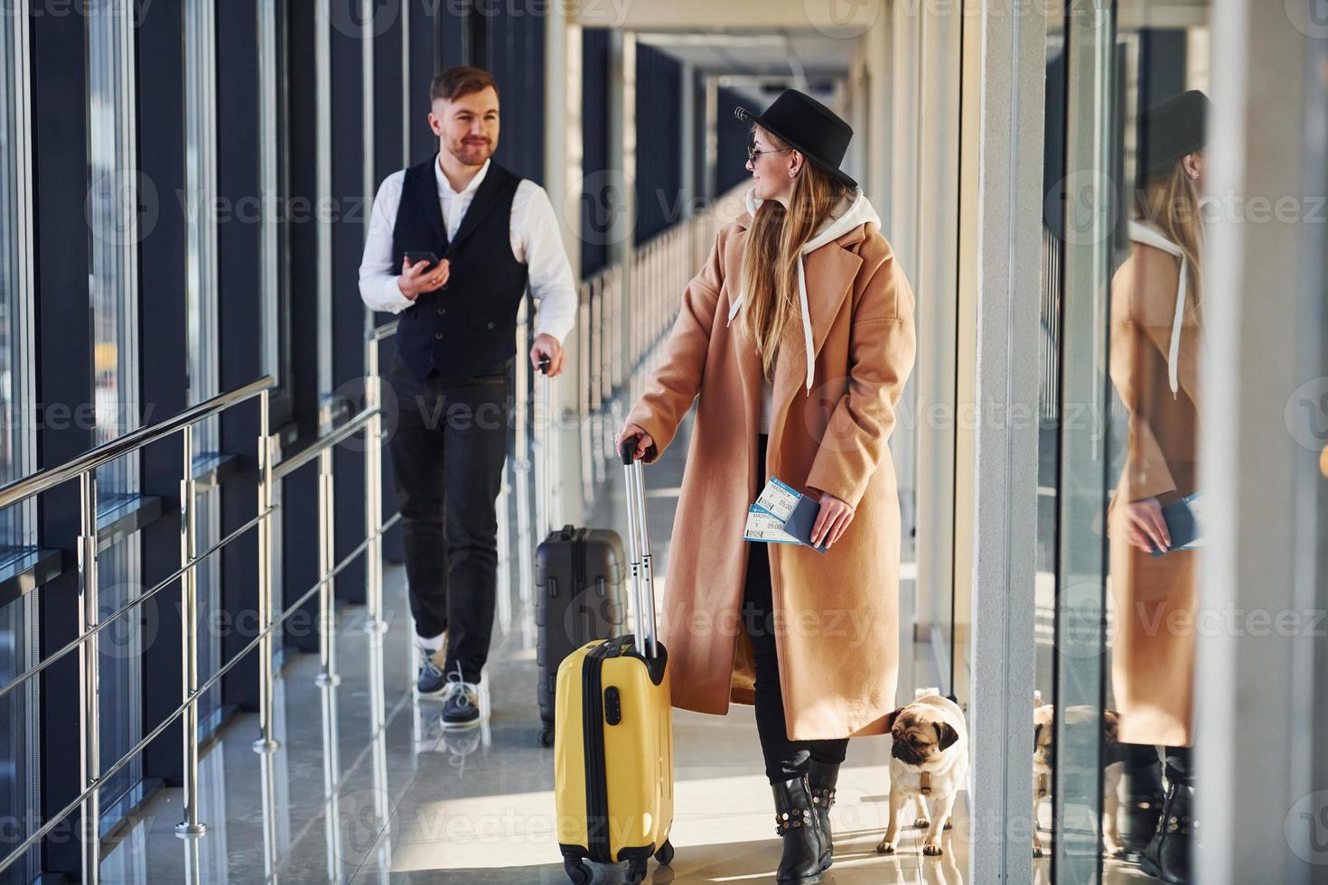 Female passenger in warm clothes, with dog and with baggage walk with man in formal wear photo