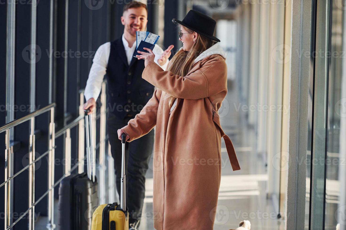 Female passenger in warm clothes, with dog and with baggage walk with man in formal wear photo