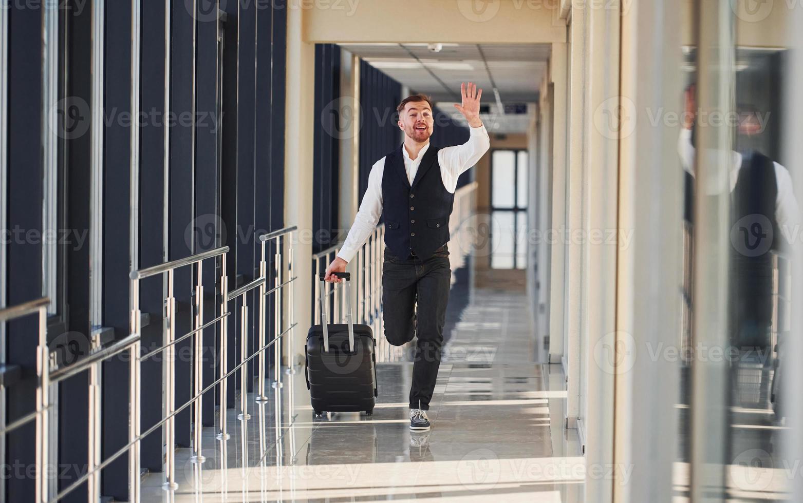Man in formal clothes and with baggage is running forward and busy for a plane photo