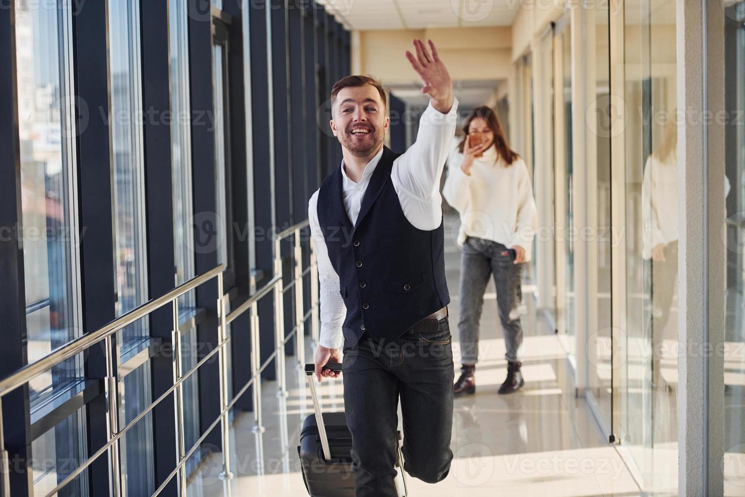 el hombre con ropa formal y con equipaje corre hacia adelante y está ocupado para un avión. chica grabándolo por teléfono foto