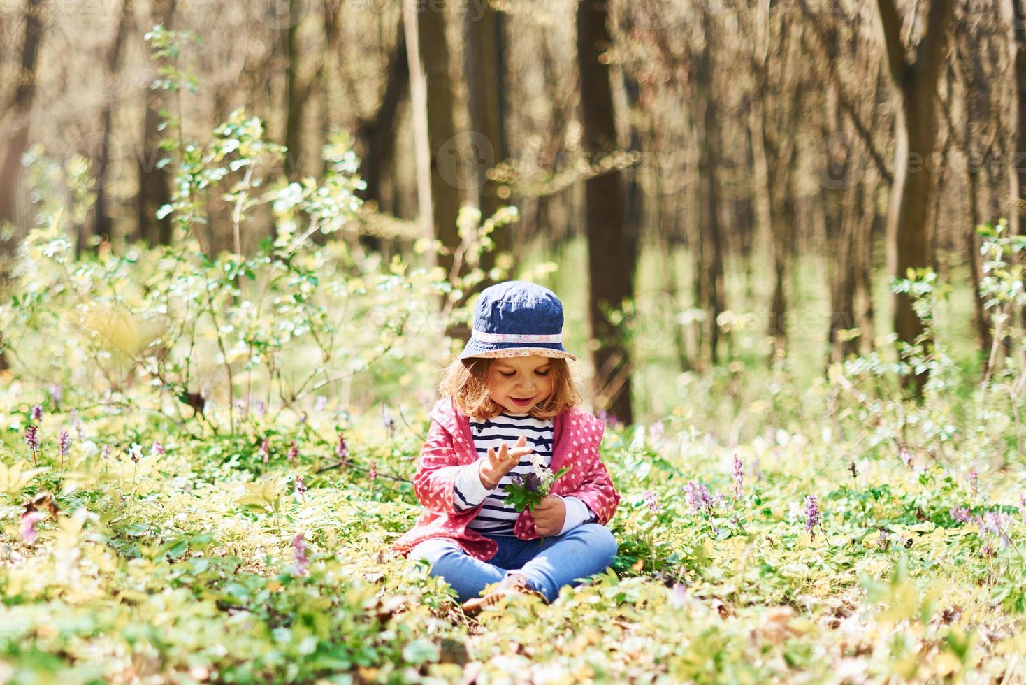Happy little girl in blue hat have walk in spring forest at daytime photo