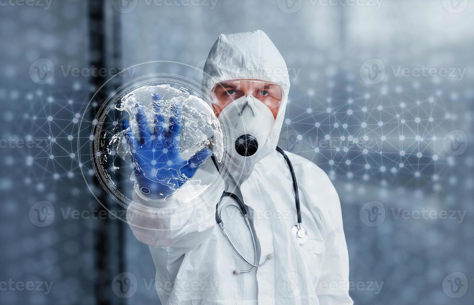 Digital world map on picture. Male doctor scientist in lab coat, defensive eyewear and mask standing indoors photo