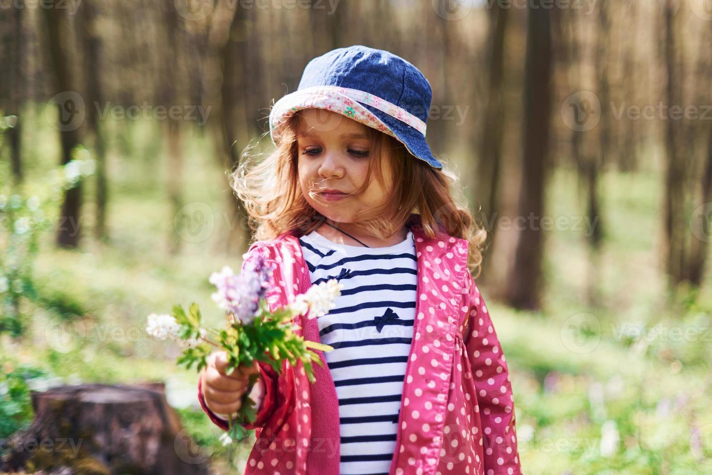 una niña feliz con sombrero azul tiene un paseo por el bosque de