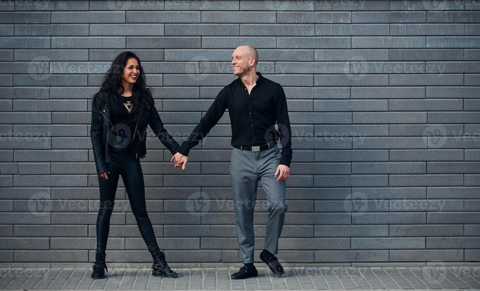 hermosa pareja vestida de negro juntos contra la pared al aire libre foto