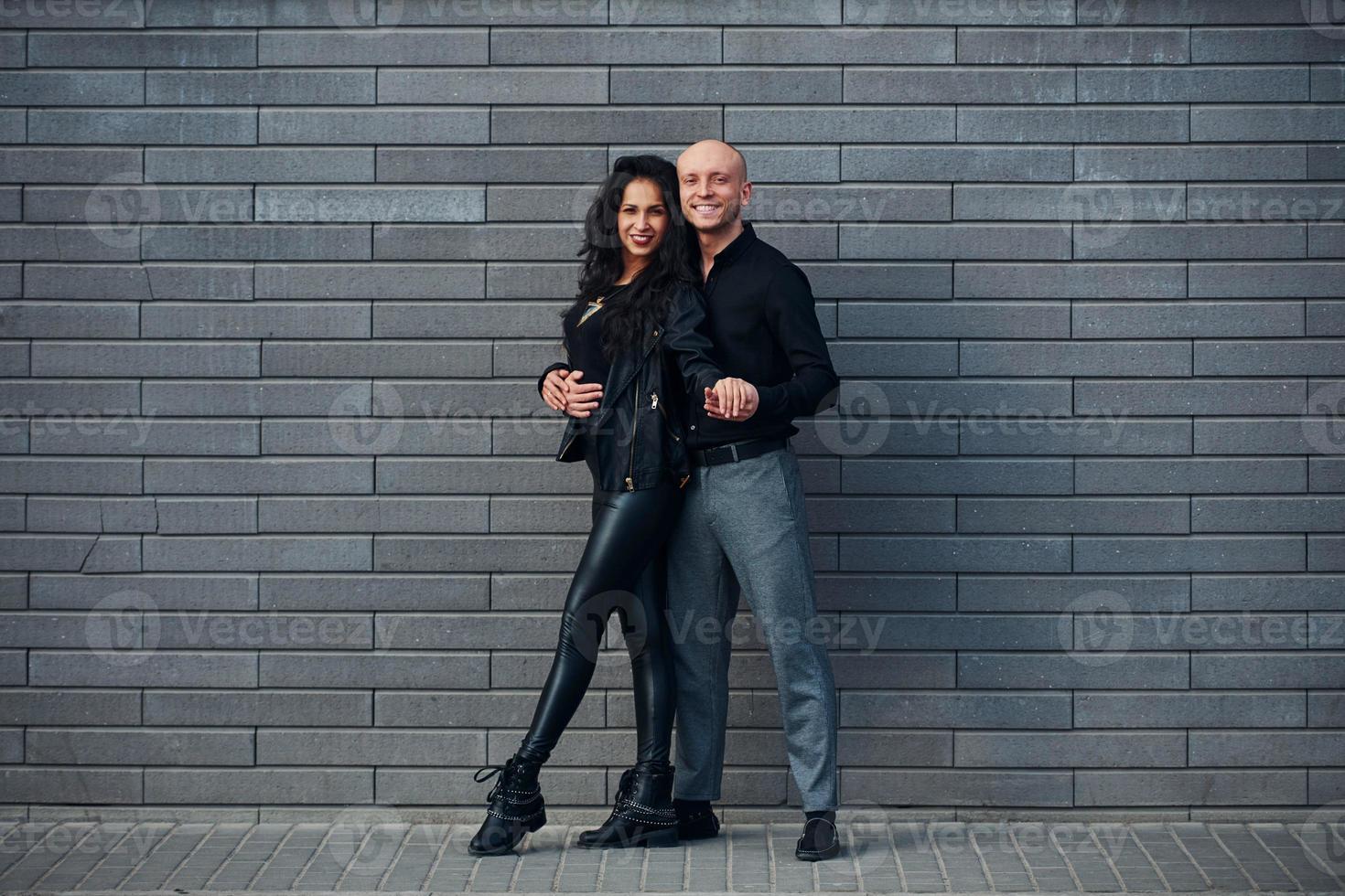 Beautiful couple in black clothes dancing together against wall outdoors photo