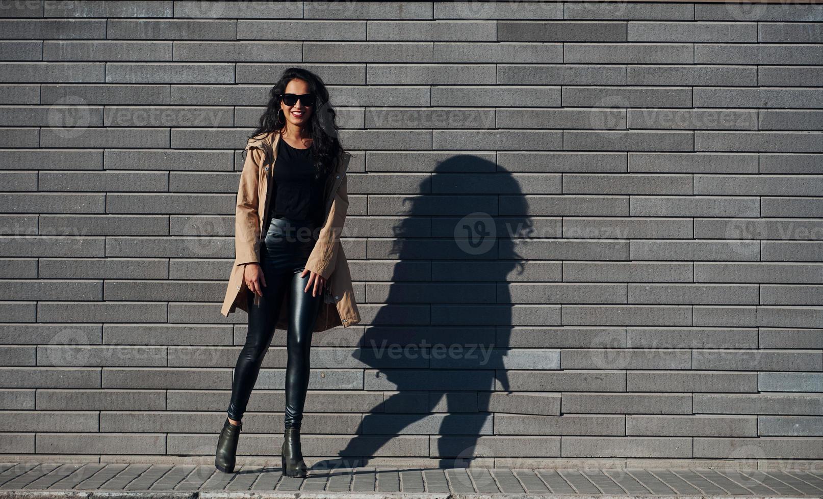 Beautiful brunette with curly hair and in black clothes outdoors near wall photo