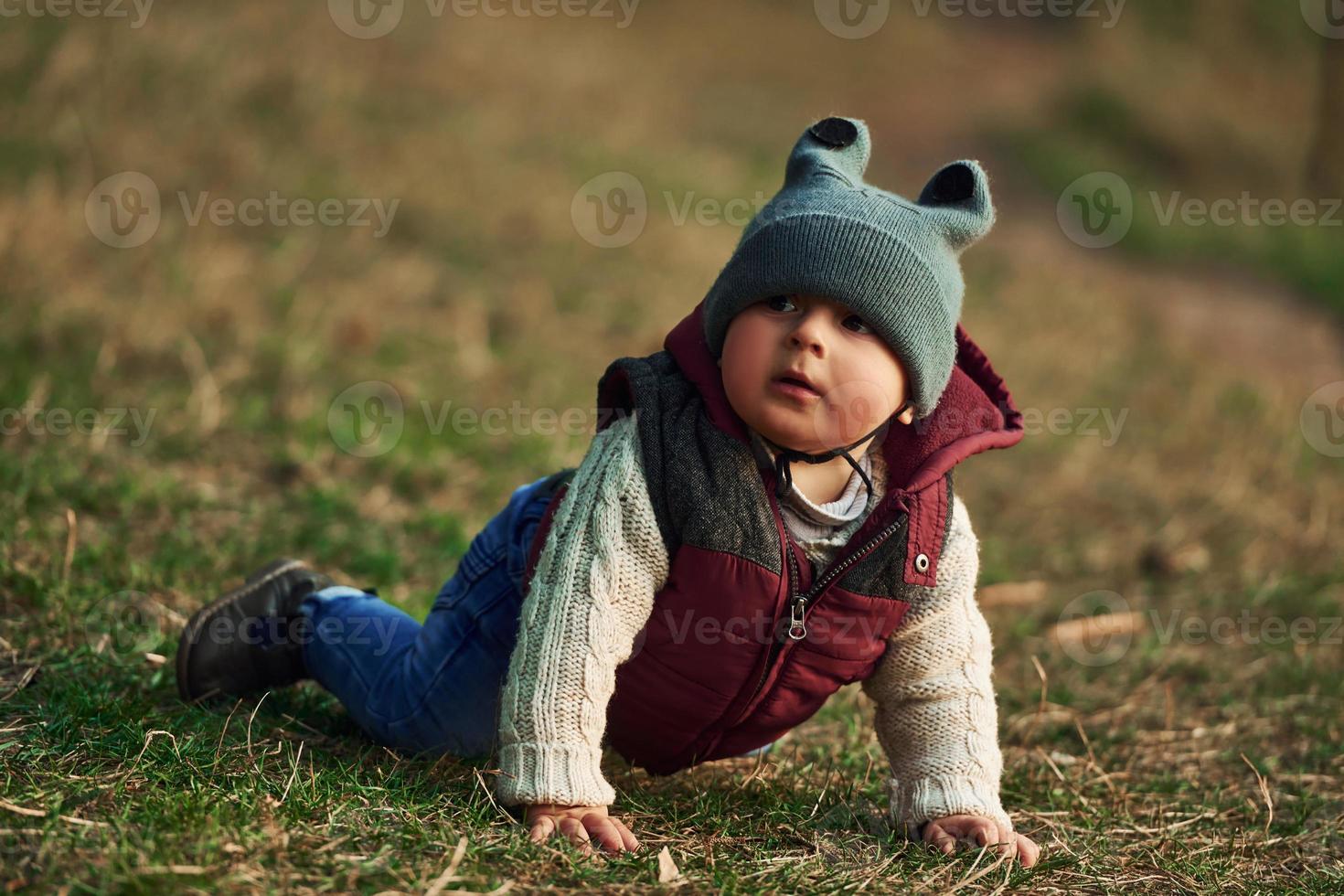 Little boy in warm clothes lying down on ground of field on grass photo
